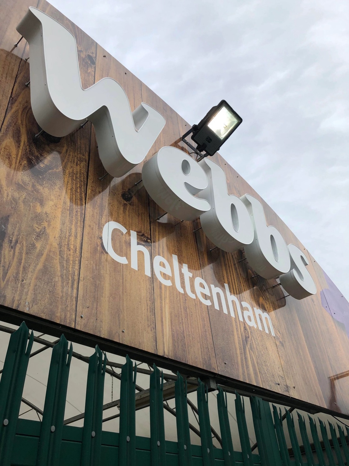 Built-up illuminated letters reading 'Webbs Cheltenham' mounted on timber cladding